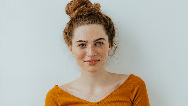 Woman portrait. Style. Beautiful blue eyed girl with freckles is looking at camera with a tender smile, on a white background