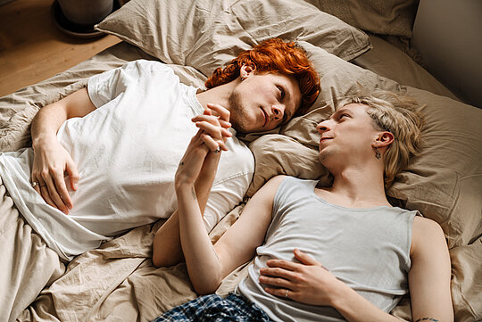Gay couple holding hands and looking at each other while laying on bed Gay couple holding hands and looking at each other while laying on bed